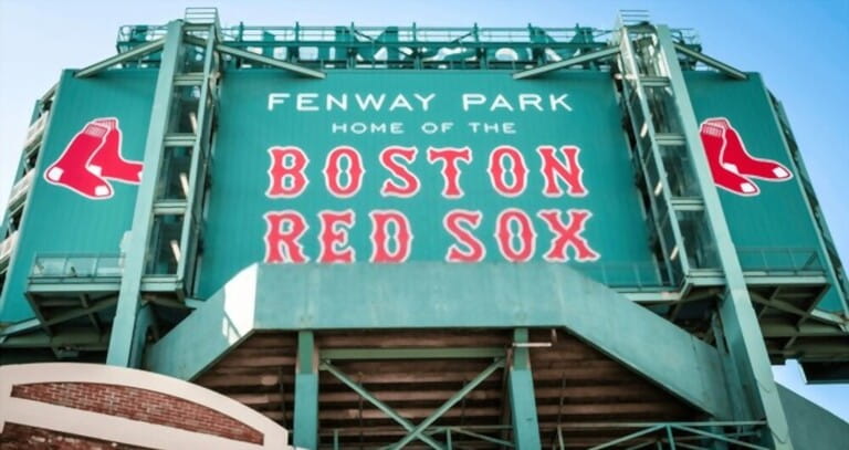 view of the historic architecture of the Fenway Park Stadium showcasing its signs, brick walls, statues, and the famous green color and red letters of the red sox.