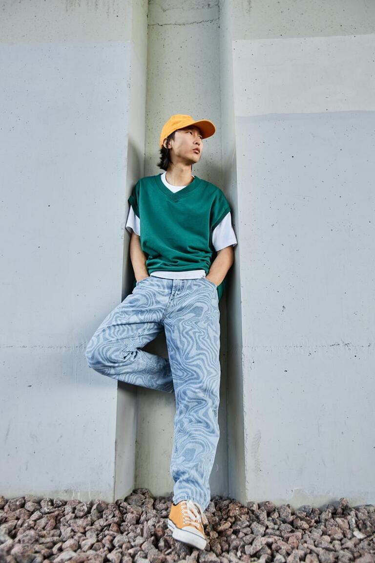Vertical portrait of young Asian man wearing colorful street style clothes standing by concrete wall in urban setting Vertical portrait of young Asian man wearing colorful street style clothes standing by concrete wall in urban setting
